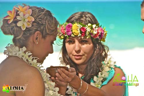 Two women in flower crowns holding a bowl of sacred red Hawaiian salt